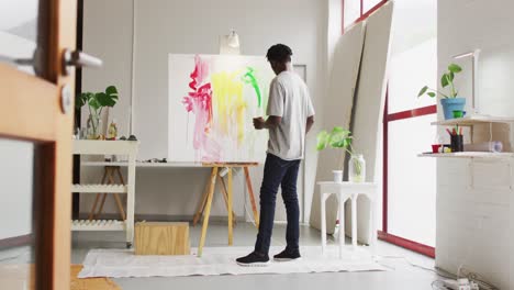 Rear-view-of-african-american-male-artist-painting-on-canvas-at-art-studio