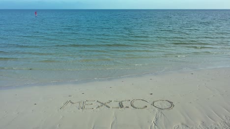 wide angle shot of mexico inscribed in the sand on a beach with a windsurfer on the horizon