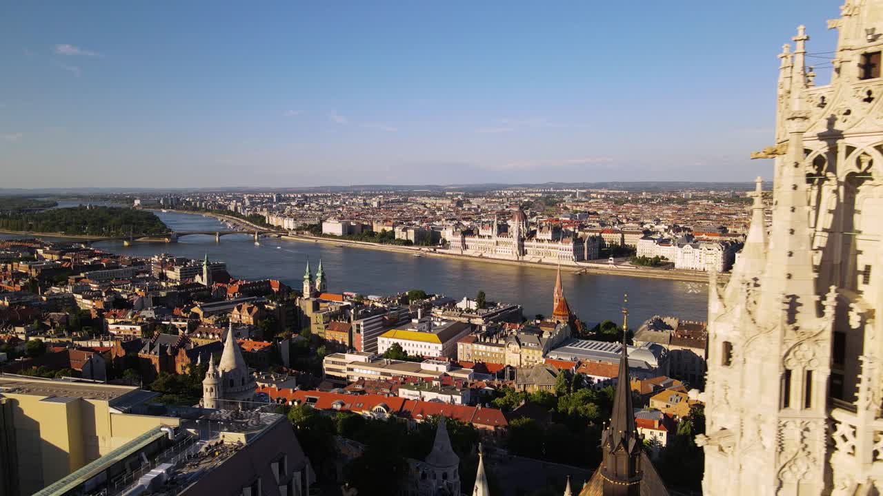 Drone che vola vicino al campanile della Chiesa di Mattia, rivelando un panorama mozzafiato di edifici iconici sulla riva del Danubio a Pest.