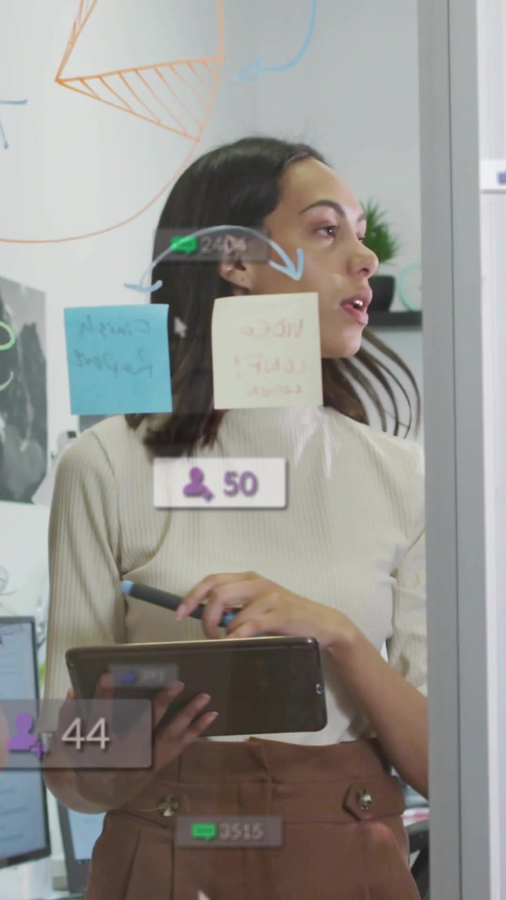 Vertical video: Tablet tapping causing UI badges on glass while woman planning business with marker