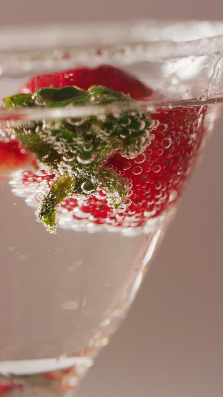 Vertical video of close up of drink with strawberries on white background