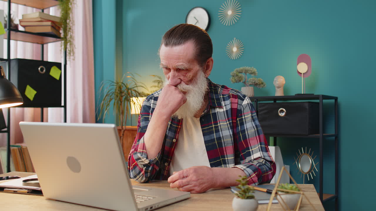 Senior man working on laptop computer at home office showing thumbs down sign dislike disapproval