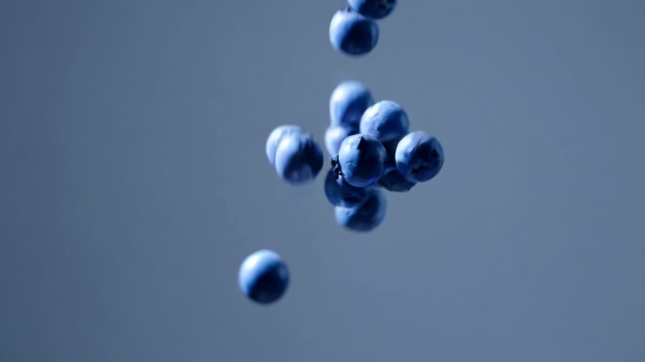 Close-up video of blueberries falling against a blue background, captured from a low angle