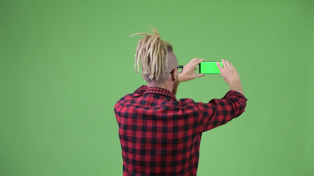 Vista Traseira de Homem Hipster Barbudo com Dreadlocks Tirando Foto com o Celular.