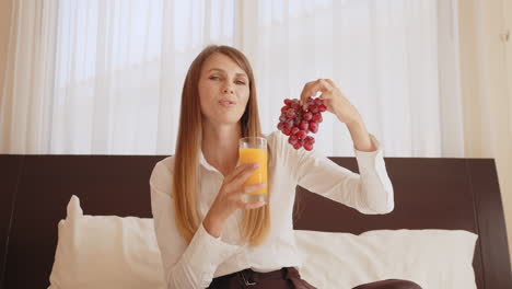 woman having breakfast in bed with orange juice and grapes