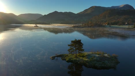 slowly approaching small island in calm lake with gentle mist moving on water surface at sunrise in autumn