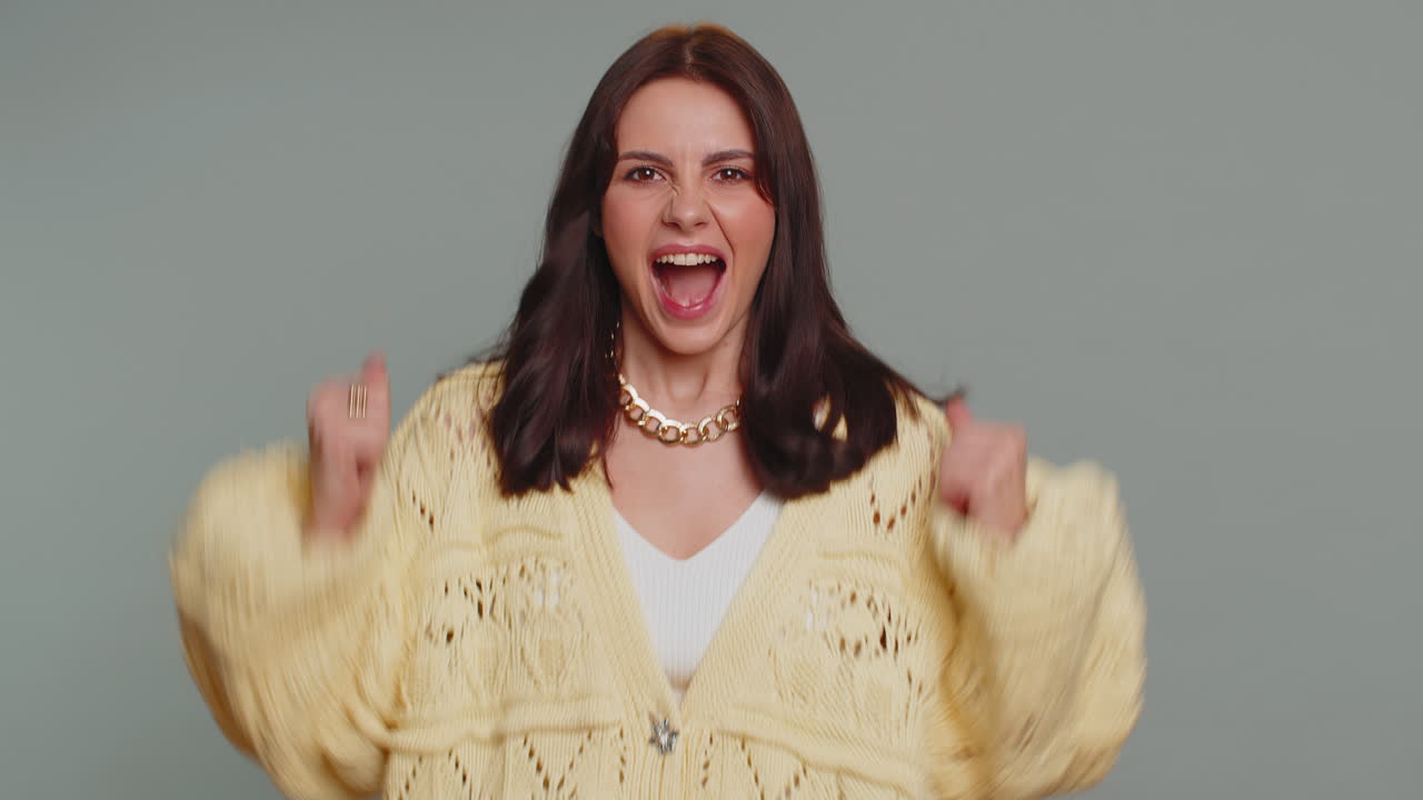 mujer elegante en cardigan gritando, levantando los puños en gesto lo hice, celebrando el éxito, ganando