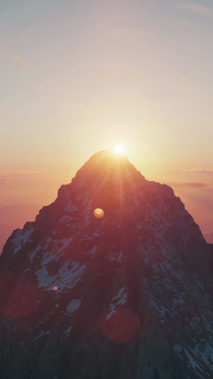 Vertical video: Rising sun reaching mountain peak, lighting snow patches and casting lens flares