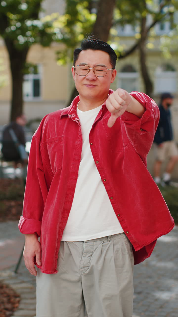 화가 난 아시아 남자가 엄지손가락을 아래로 보여주는 표시, 불쾌감, 불만족, 나쁜 일, 도시에서 실수