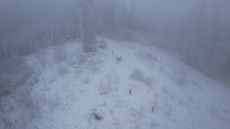 Vista-Aérea-De-La-Gente-Que-Llega-A-La-Torre-De-Vigilancia-En-Una-Colina-Cubierta-De-Nieve-Bajo-La-Niebla