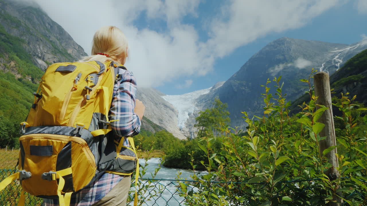 un turista con una mochila amarilla mira un hermoso glaciar en la cima de la montaña briksdal gl