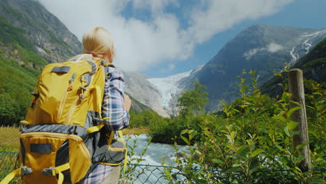 a tourist with a yellow backpack looks at a beautiful glacier at the top of the mountain briksdal gl