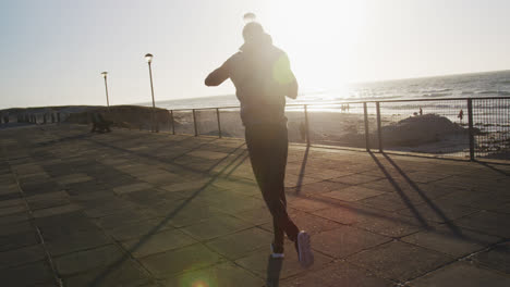 Focused-african-american-man-boxing-and-running,-exercising-outdoors-by-the-sea