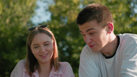 couple conversing happily outdoors with woman wearing glasses on her head, both smiling and enjoying the moment, surrounded by greenery in the background