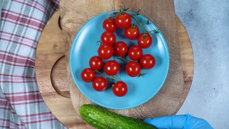 circular rotation a bunch of cherry tomatoes and woman's hand in a rubber glove places two cucumbers on a plate.