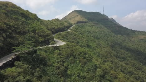 aerial follows motorcycle up lush, green hill station road in india