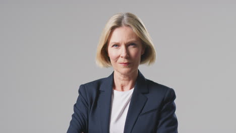Studio-Portrait-Of-Mature-Businesswoman-With-Serious-Expression-Standing-Against-Plain-Background