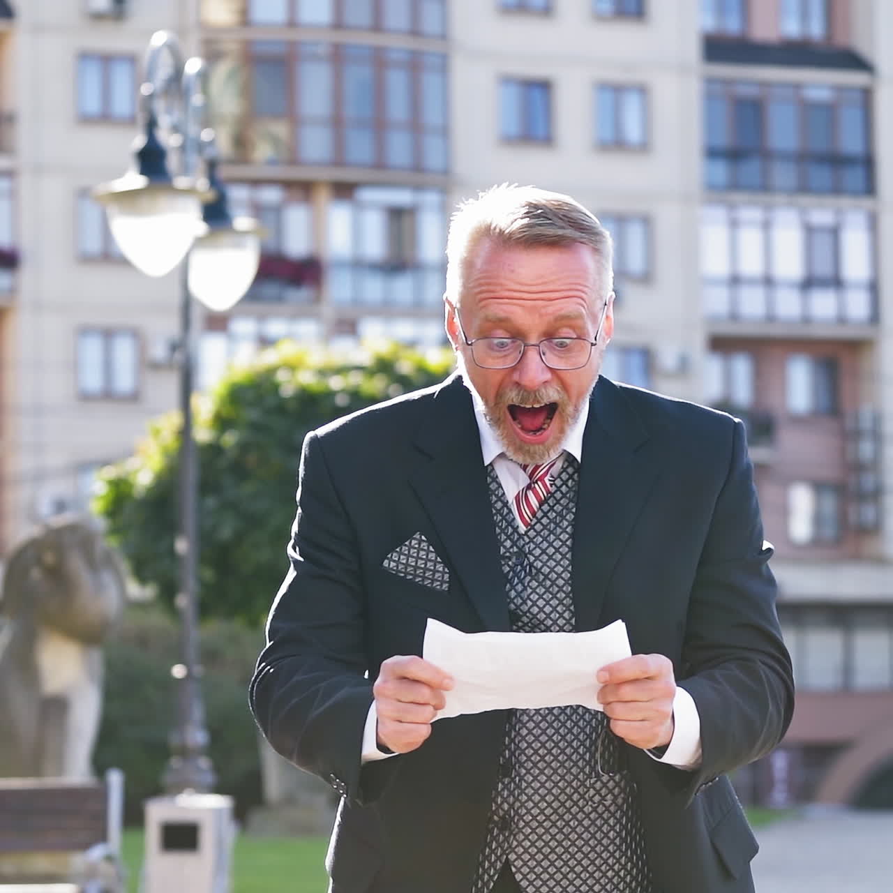 Mature businessman with a sheet of paper on the city background. Portrait of an old man in elegant costume reading paper and becomes very happy outdoors.