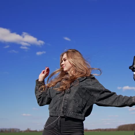 attractive pop singer dances outdoors. beautiful young blonde woman in jeans clothes singing into the microphone on the sky background