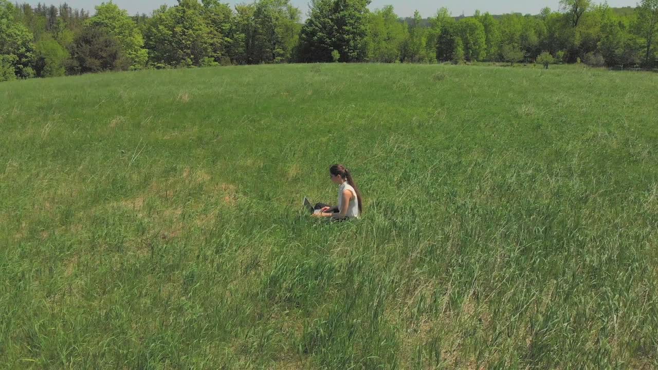 젊은 여성이 잔디에서 노트북에서 일하고 있습니다.