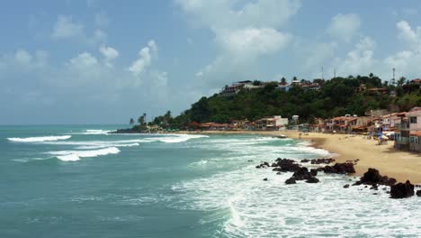 dolly en toma aérea de drones de la famosa ciudad de playa tropical de baia formosa en el estado de rio grande do norte, brasil con barcos de pesca, casas costeras, olas pequeñas y surfistas
