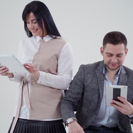 young couple with modern devices in studio. smiling woman looking at digital tablet. handsome man sitting in chair and watching video on tablet.
