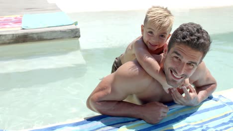 Portrait-of-happy-caucasian-father-carrying-his-son-with-towel-at-swimming-pool