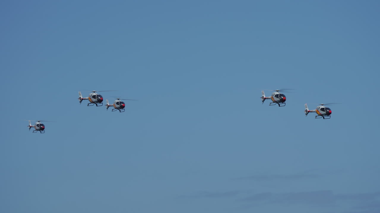 Four helicopters flying in close synchronized formation against a clear blue sky