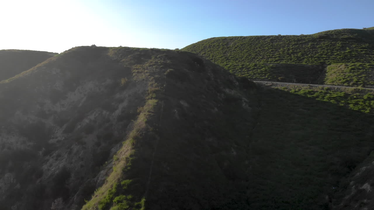 Winding highway bends through empty rolling hills covered in green grass as seen from above aerial as cars and trucks travel and ship.