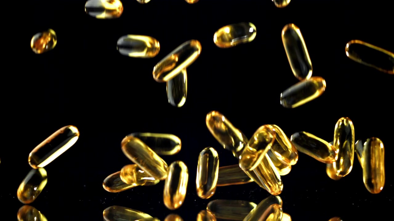 Capsule softgel dorate che cadono al rallentatore su sfondo nero riflettente