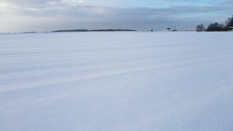 Drone-shot-of-empty-field-covered-with-snow-with-visible-footprints-in-the-winter