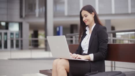 Woman-sitting-with-laptop-on-bench-outdoors