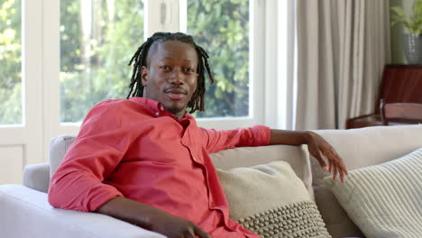 portrait of happy african american man with dreadlocks smiling on couch in sunny room, slow motion