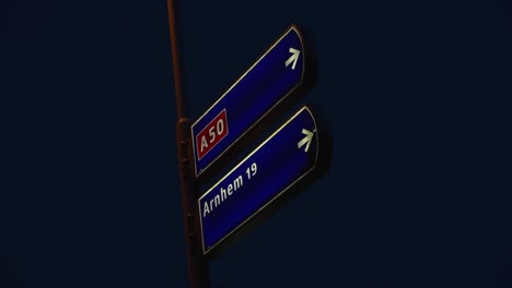 Night view of road signs indicating direction to Arnhem via A50