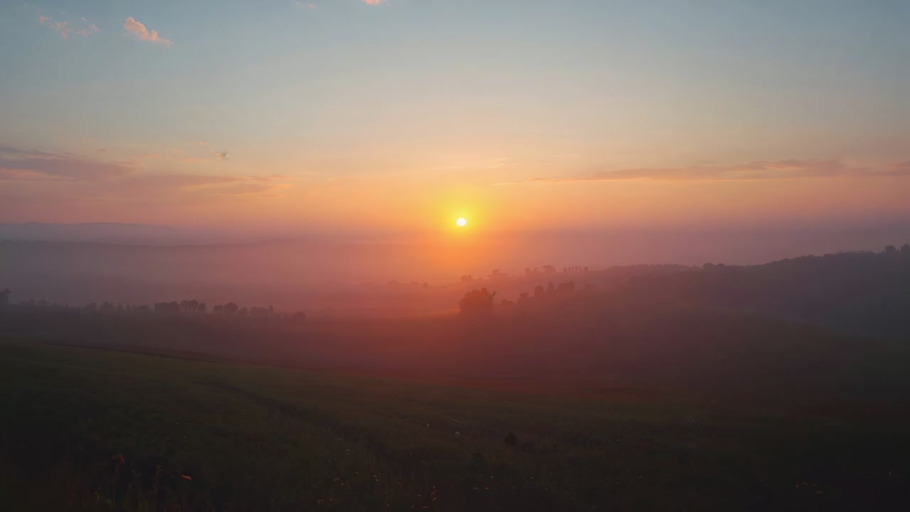 Stigende sol lyser opp himmelen over en tåkete dal mens morgengryets lys intensiveres, med tynne skyer og åser.