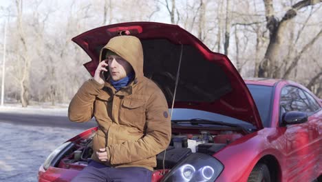 Man-in-winter-coat-stands-near-the-broken-down-car-and-calls-for-help