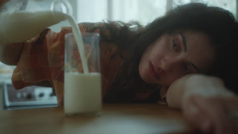 young tired woman resting her head on kitchen table, filling glass with milk