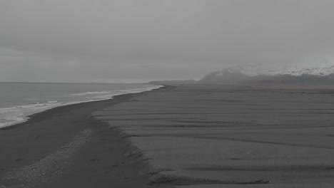 reversing flyover black sand beach with mountainous backdrop