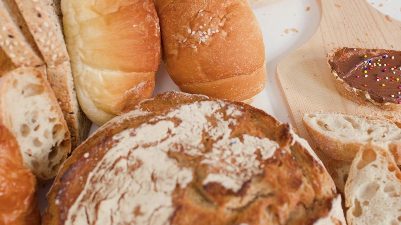 Close-up overhead shot of sourdough, baguettes, and croissants with chocolate spread on wood.