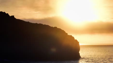 silhouetted cliff against sunset sky with clouds, drone view