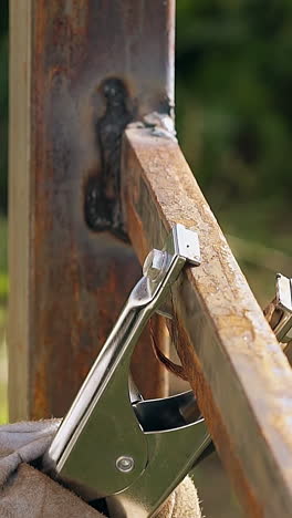 close view handyman in camouflage workwear takes away metal clamp from fixed plank on fence
