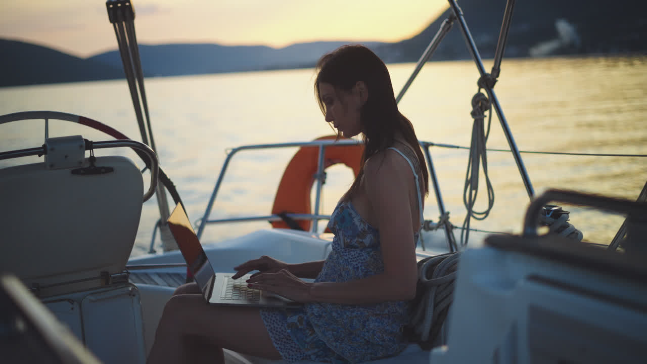 mujer trabajando en una computadora portátil en un yate durante el atardecer