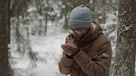 man warming his hands in a snowy forest