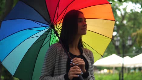 Portrait-of-a-young-beautiful-happy-woman-walking-and-spinning-her-colorful-umbrella-in-a-rainy-day-in-the-city-park