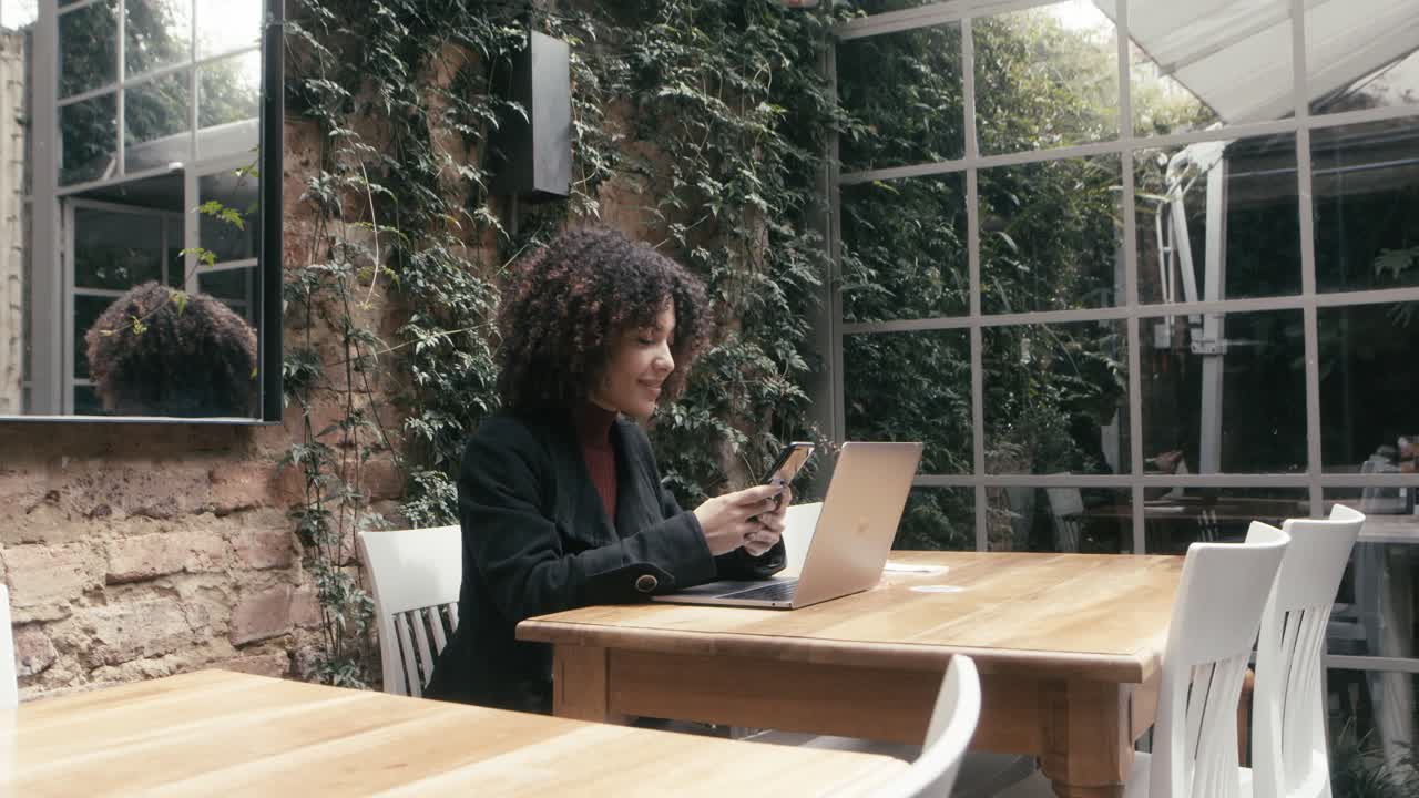 A woman in a suit sits in a cafe while opening her laptop to complete work from her office
