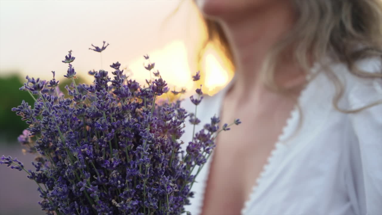 Close up of a woman in a white dress holding a bouquet of lavender in a field at sunset