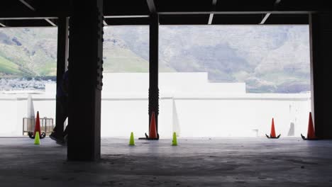 Hombre-Afroamericano-Haciendo-Slalom-Con-Una-Pelota-De-Fútbol-En-Un-Edificio-Urbano-Vacío