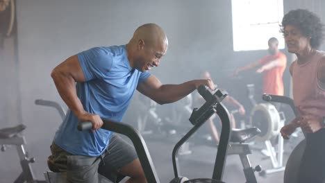 Vielfältige-Trainerin-Motiviert-Entschlossenen-Mann,-Der-Hart-Auf-Dem-Crosstrainer-Im-Fitnessstudio-Trainiert,-Zeitlupe