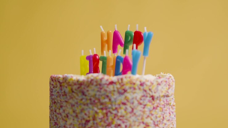 Studio Shot Of Revolving Birthday Cake Covered With Decorations And Candles Spelling Out Happy Birthday 2