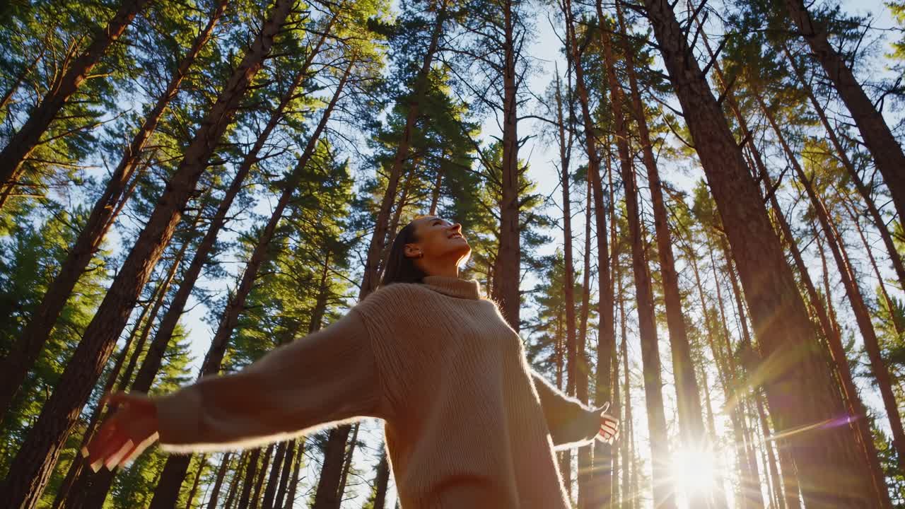 Low-angle video shot of a woman in a forest, arms outstretched, embracing nature
